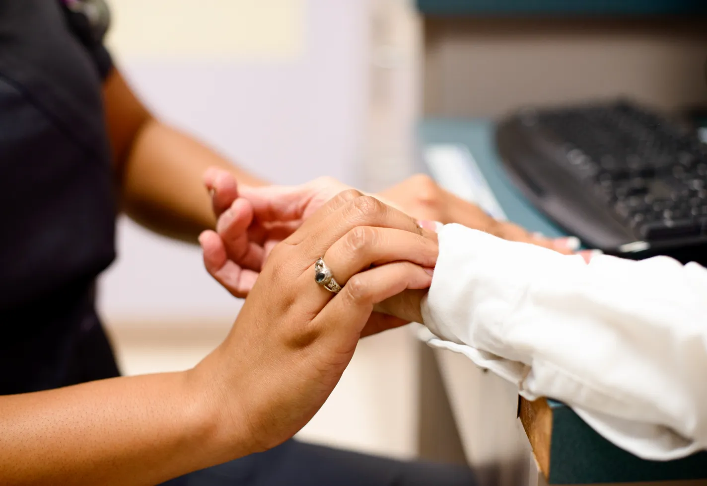 Nurse and patient are sitting across from each other in a clinic exam room. The nurse holds and positions the patients hands to check for their pulse. 